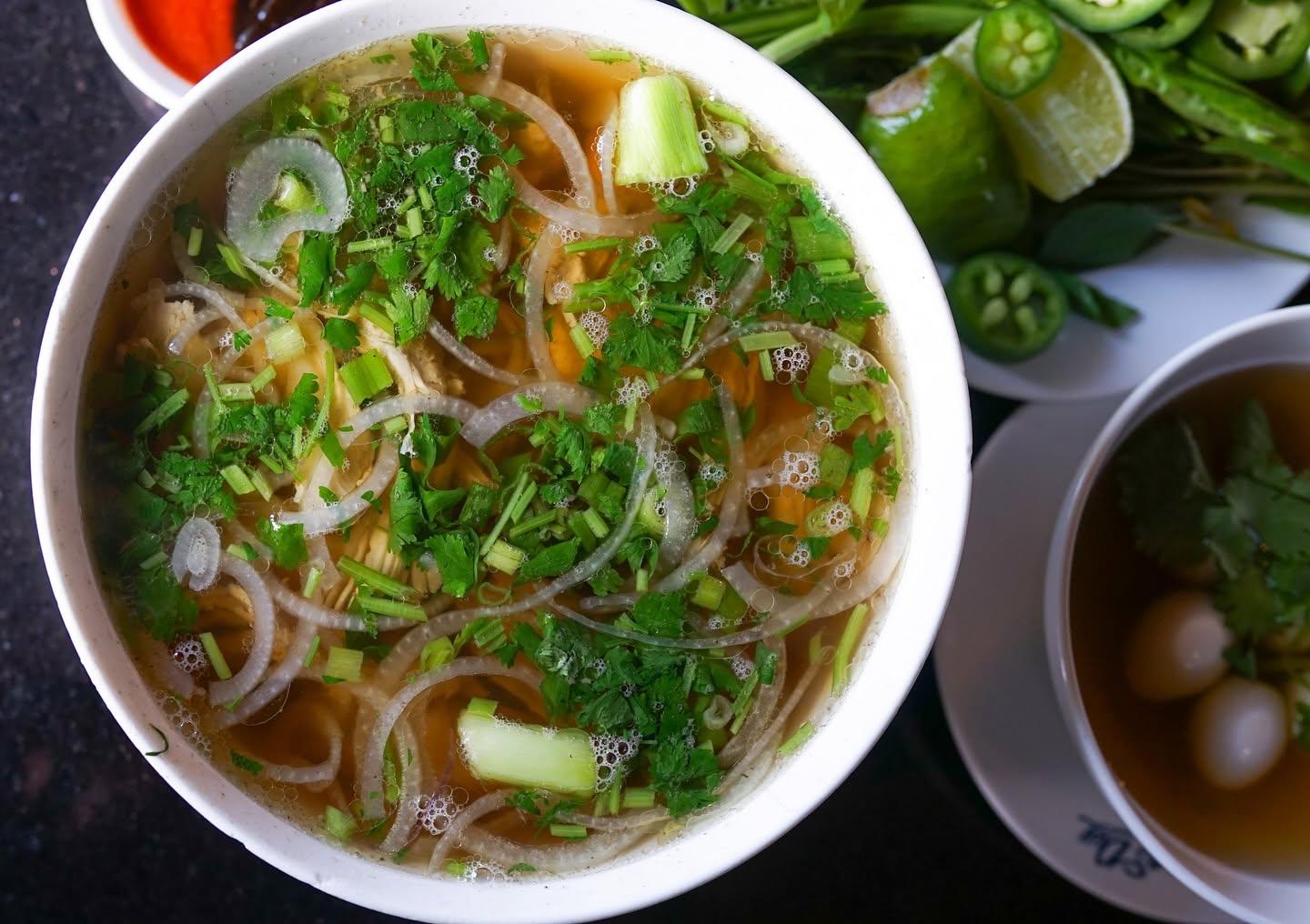 Bowl of chicken pho with onions, herbs, and a side of quail eggs