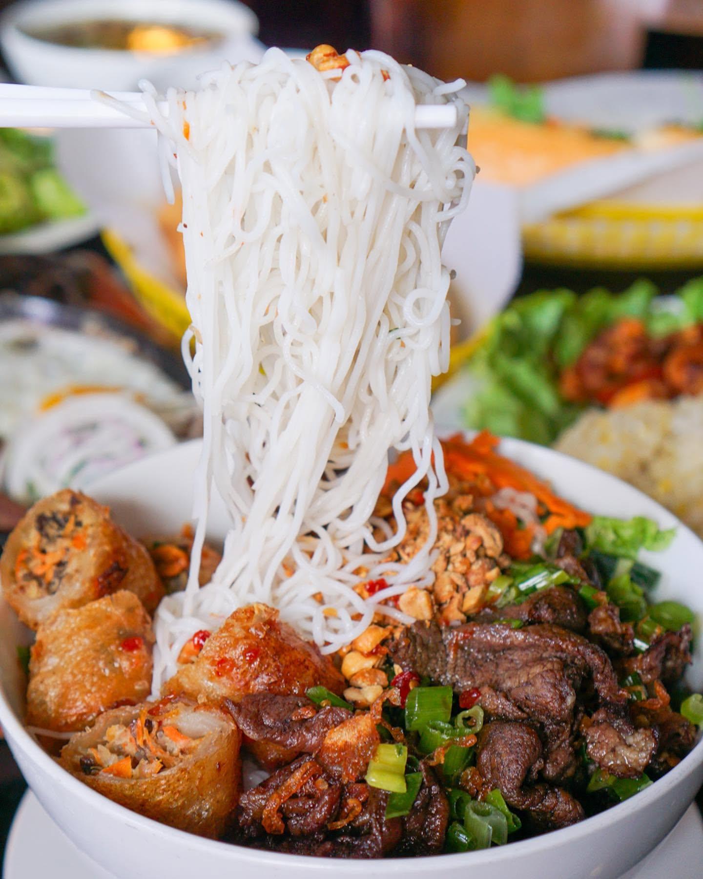 Vermicelli noodles lifted from a bowl with egg rolls and grilled meat