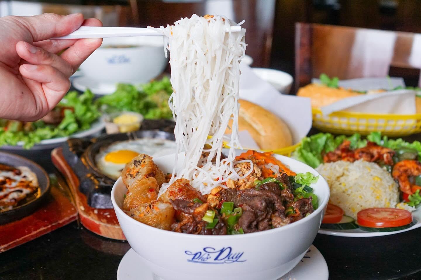 Pho Duy vermicelli bowl with egg rolls, grilled meat, and pickled vegetables